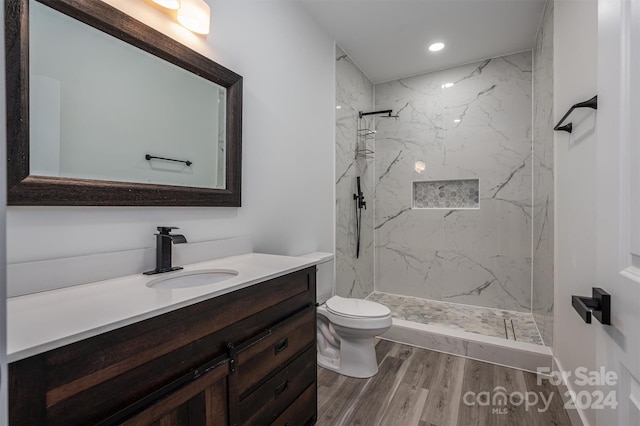 bathroom with hardwood / wood-style flooring, vanity, toilet, and a tile shower