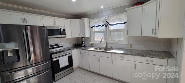 kitchen with appliances with stainless steel finishes, ornamental molding, sink, stone countertops, and white cabinetry