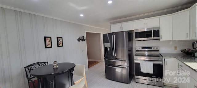 kitchen featuring light stone counters, appliances with stainless steel finishes, decorative backsplash, white cabinets, and ornamental molding