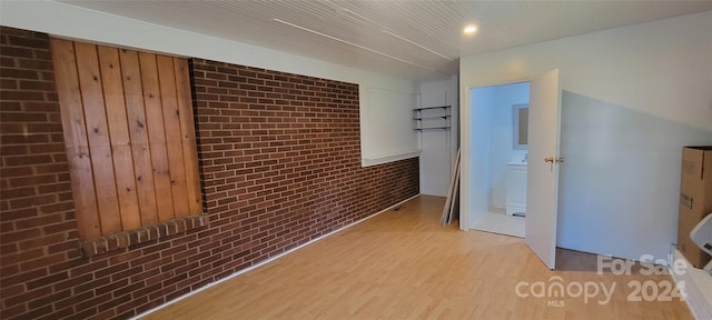 corridor featuring light wood-type flooring and brick wall