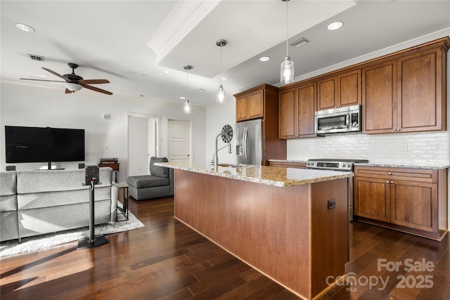 kitchen with a kitchen island with sink, pendant lighting, stainless steel appliances, and light stone counters