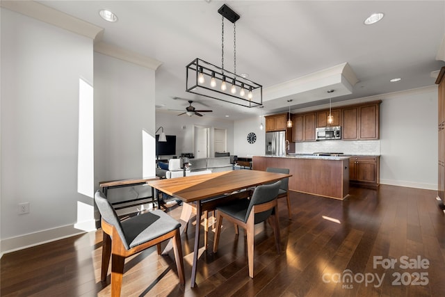 dining space featuring a raised ceiling, ceiling fan, dark wood-type flooring, and ornamental molding