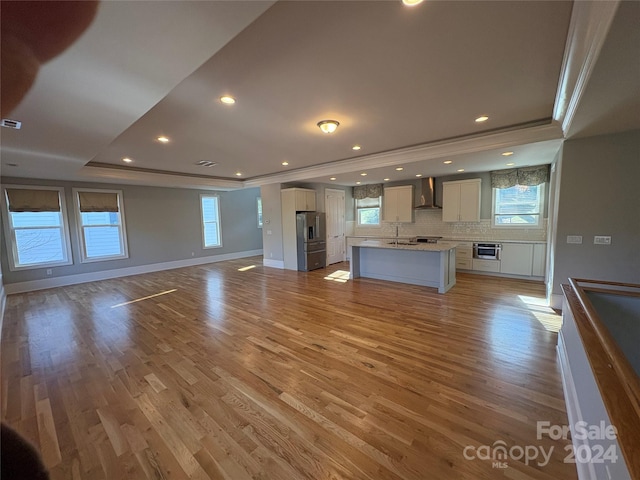 kitchen with stainless steel fridge, light hardwood / wood-style flooring, a healthy amount of sunlight, and wall chimney range hood