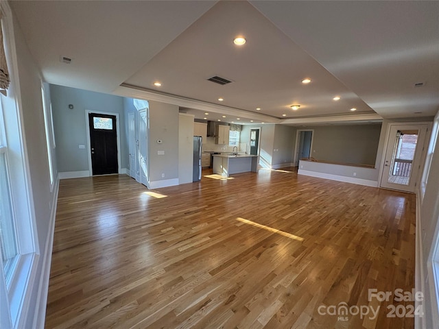 unfurnished living room with a tray ceiling, hardwood / wood-style floors, and sink