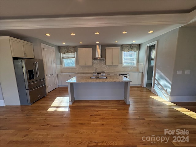 kitchen with backsplash, a center island with sink, wall chimney range hood, hardwood / wood-style flooring, and stainless steel appliances