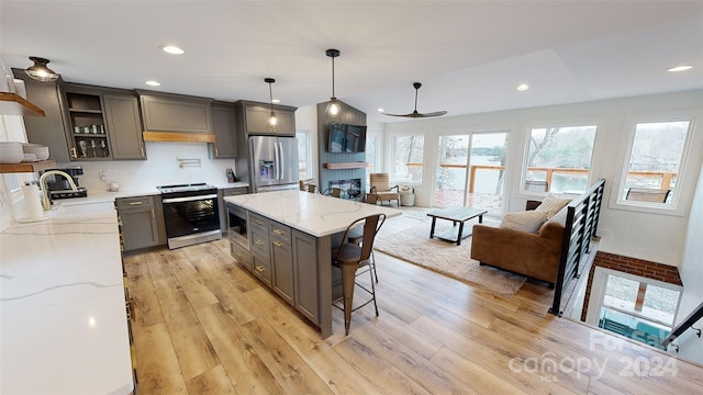 kitchen featuring hanging light fixtures, light hardwood / wood-style flooring, light stone countertops, a kitchen island, and stainless steel appliances