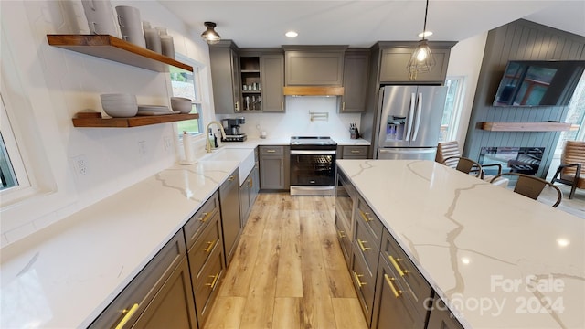 kitchen with sink, hanging light fixtures, light stone countertops, appliances with stainless steel finishes, and light hardwood / wood-style floors