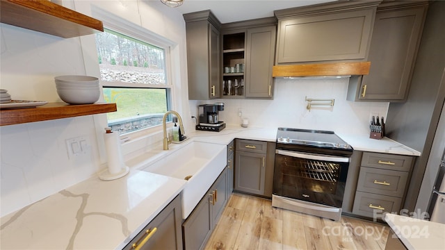 kitchen featuring light wood-type flooring, stainless steel electric range oven, sink, and tasteful backsplash