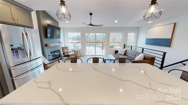 kitchen with hanging light fixtures, ceiling fan, gray cabinets, light stone counters, and stainless steel fridge with ice dispenser