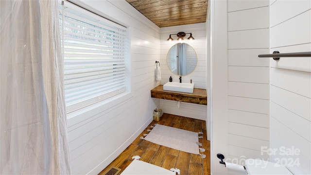 bathroom featuring wooden walls, hardwood / wood-style flooring, wooden ceiling, and sink