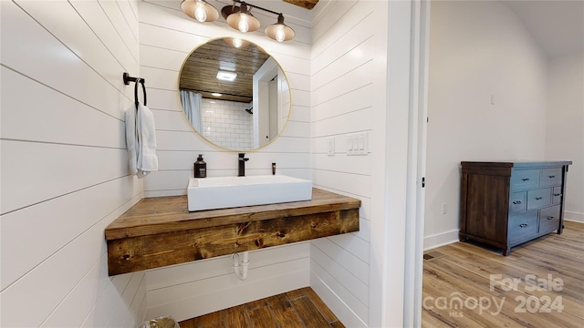 bathroom with hardwood / wood-style flooring, wooden walls, and sink