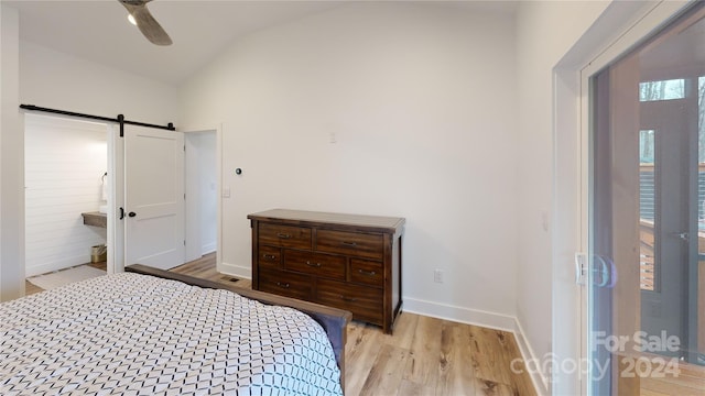 bedroom with ceiling fan, a barn door, light wood-type flooring, and vaulted ceiling