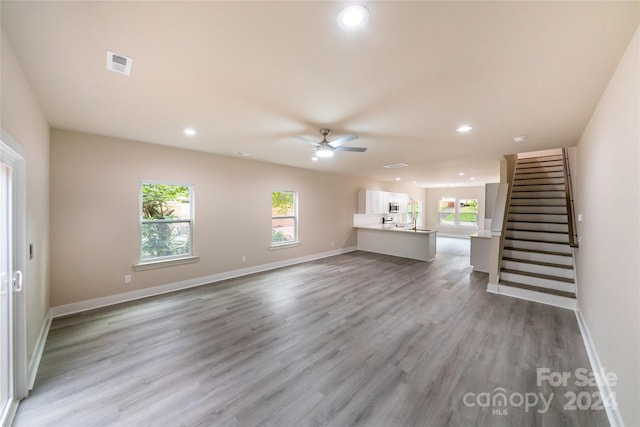 unfurnished living room featuring a wealth of natural light, ceiling fan, and light wood-type flooring