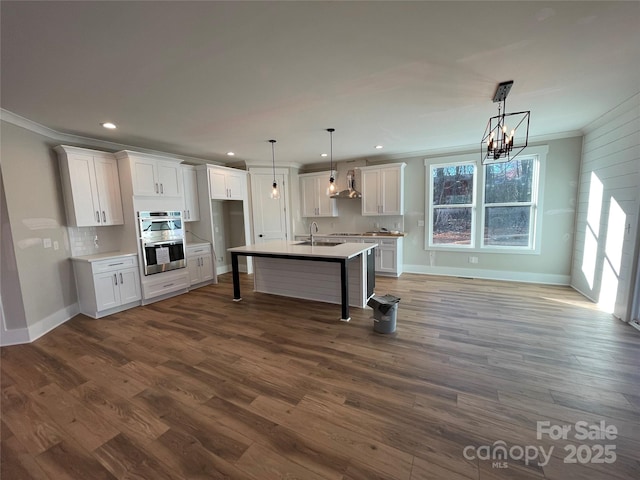 kitchen featuring wall chimney range hood, ornamental molding, dark wood finished floors, and a sink