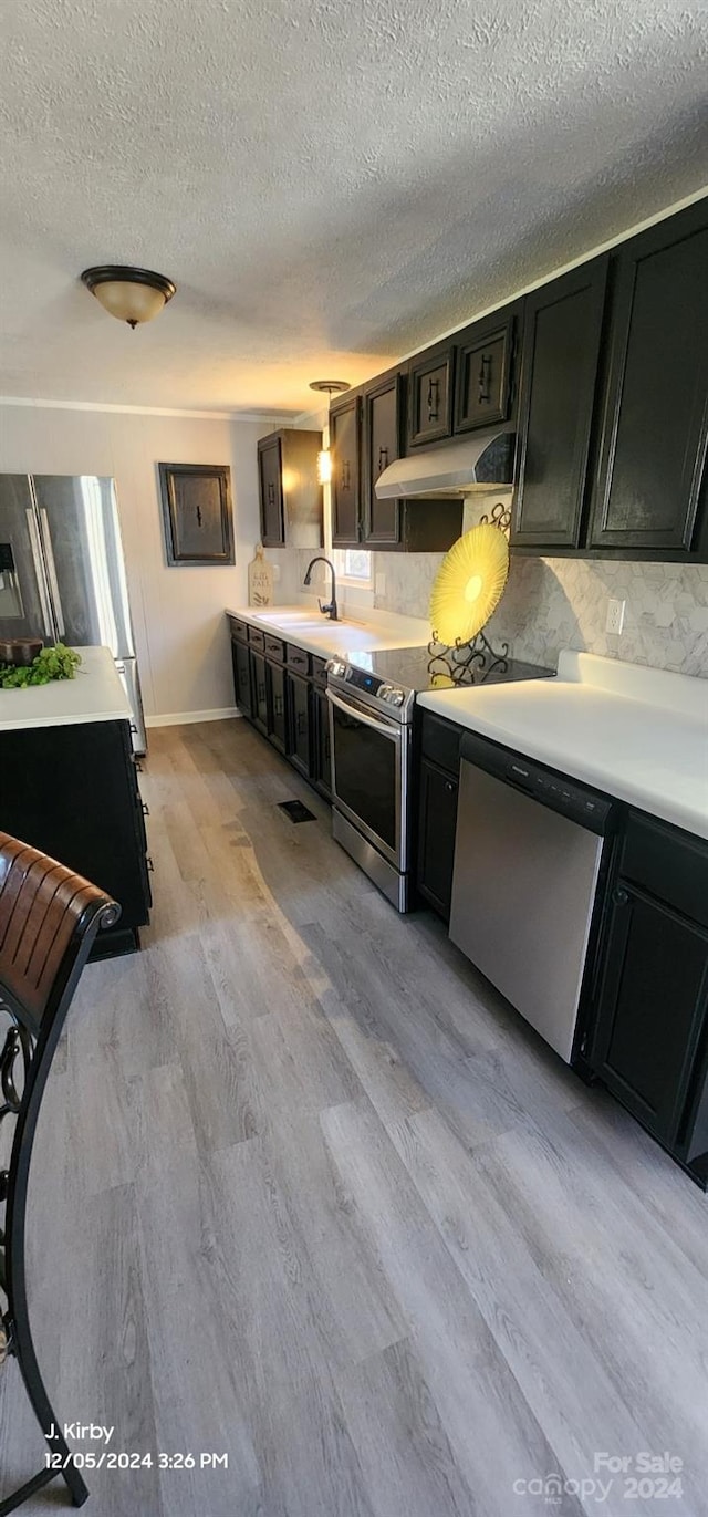 kitchen with backsplash, sink, light wood-type flooring, a textured ceiling, and appliances with stainless steel finishes