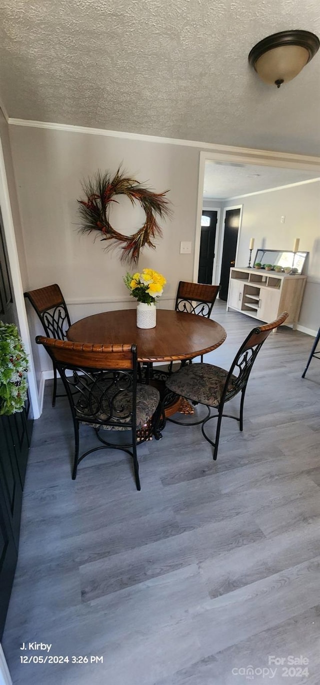 dining room with hardwood / wood-style floors, a textured ceiling, and crown molding