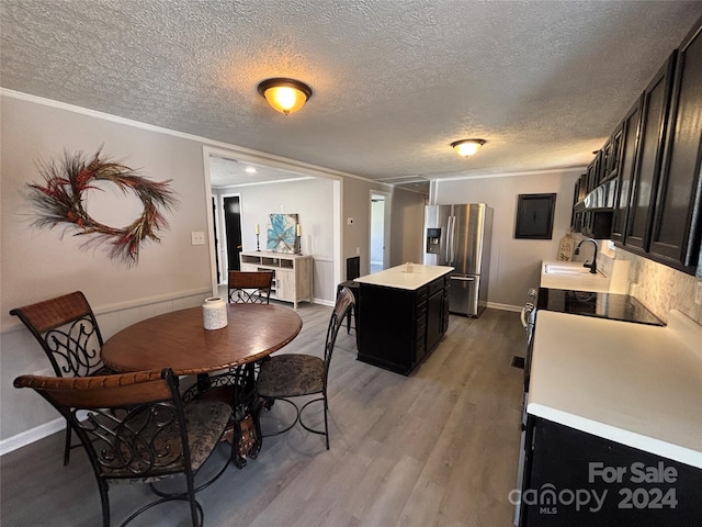 dining space with a textured ceiling, ornamental molding, sink, and light hardwood / wood-style flooring