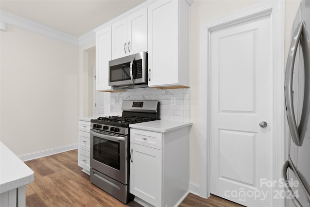 kitchen with backsplash, ornamental molding, stainless steel appliances, wood-type flooring, and white cabinets