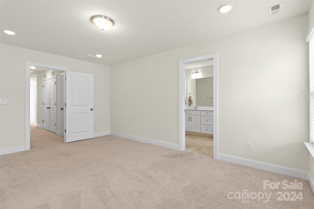 unfurnished bedroom with ensuite bathroom and light colored carpet