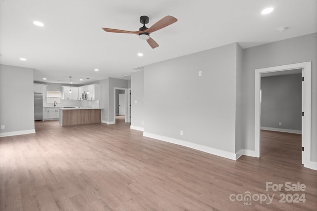 unfurnished living room featuring ceiling fan, light wood-type flooring, and sink