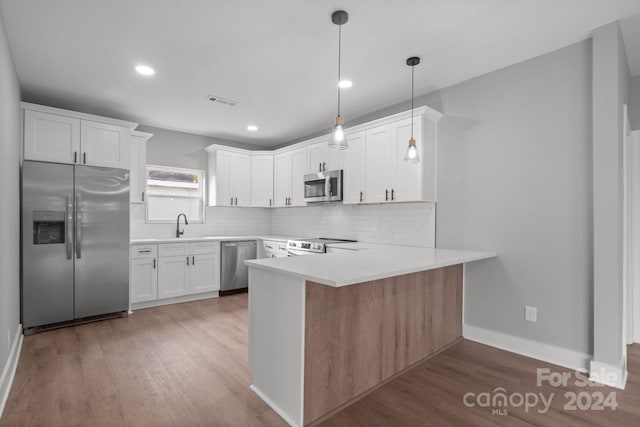 kitchen with kitchen peninsula, appliances with stainless steel finishes, dark hardwood / wood-style flooring, decorative light fixtures, and white cabinets