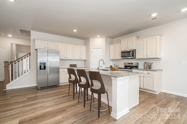 kitchen featuring light stone counters, light wood-type flooring, stainless steel appliances, and an island with sink