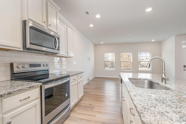 kitchen with light stone countertops, stainless steel appliances, light hardwood / wood-style floors, and sink