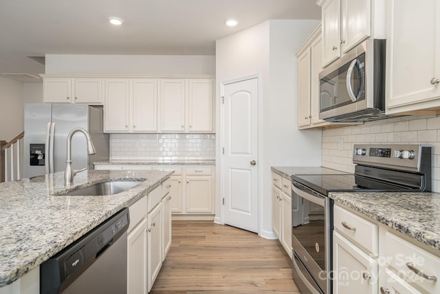 kitchen with light hardwood / wood-style floors, light stone countertops, sink, and appliances with stainless steel finishes