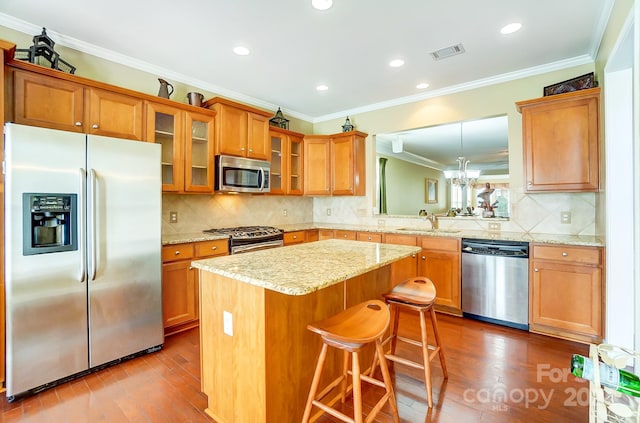 kitchen featuring appliances with stainless steel finishes, ornamental molding, wood-type flooring, a center island, and a breakfast bar area