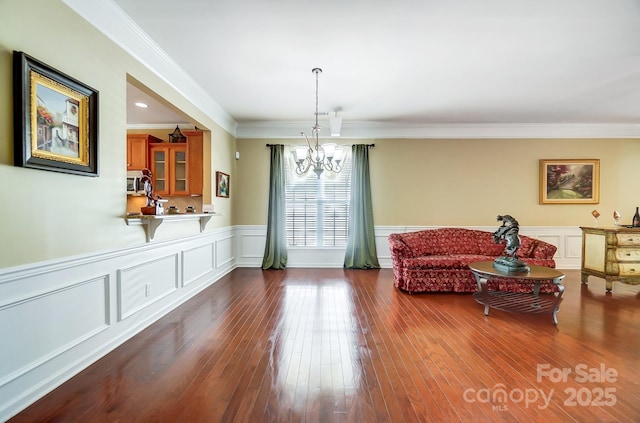 sitting room featuring dark wood finished floors, a notable chandelier, a decorative wall, and crown molding