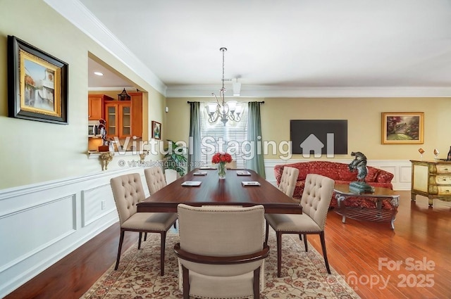 dining area with wood finished floors, a wainscoted wall, crown molding, a decorative wall, and a notable chandelier