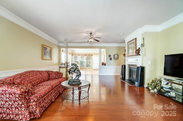 living room featuring wood finished floors, ornate columns, a fireplace with flush hearth, ornamental molding, and a decorative wall