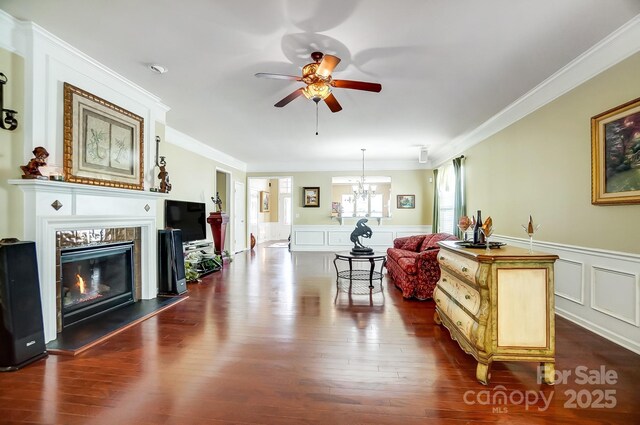 living room with wainscoting, dark wood-type flooring, a glass covered fireplace, and crown molding