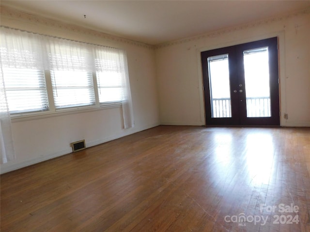 empty room with french doors, a wealth of natural light, and hardwood / wood-style floors