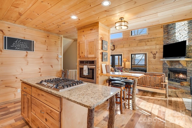 kitchen featuring light stone countertops, wooden walls, light wood-type flooring, and appliances with stainless steel finishes