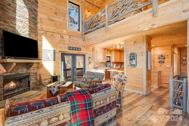 living room with french doors, light wood-type flooring, wooden walls, a fireplace, and a high ceiling