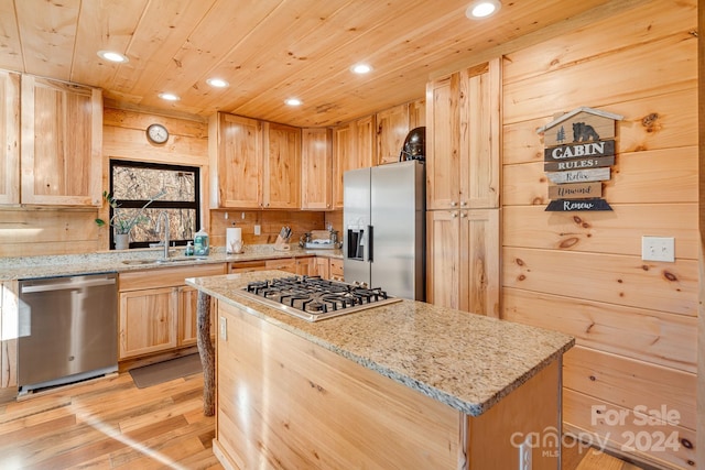 kitchen with sink, light wood-type flooring, a kitchen island, light stone counters, and stainless steel appliances