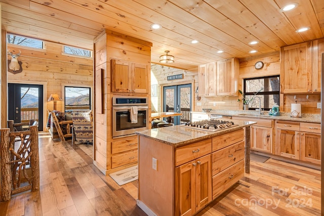 kitchen featuring french doors, light stone counters, stainless steel appliances, light hardwood / wood-style floors, and wood walls