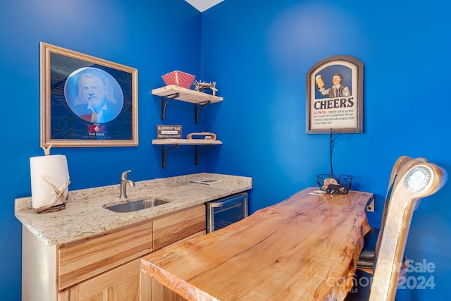 interior space with light brown cabinetry, light stone counters, wine cooler, and sink