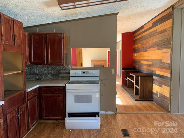 kitchen featuring a textured ceiling, electric range, light hardwood / wood-style floors, lofted ceiling, and wood walls