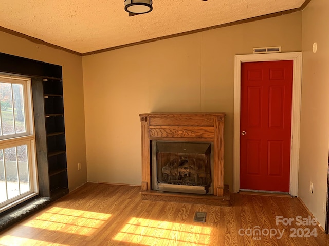 unfurnished living room with hardwood / wood-style flooring, built in shelves, crown molding, and a textured ceiling