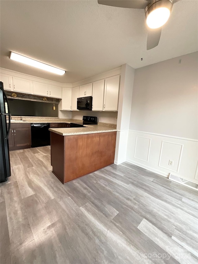 kitchen with ceiling fan, kitchen peninsula, light hardwood / wood-style floors, white cabinets, and black appliances