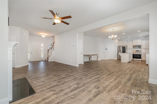 unfurnished living room with ceiling fan with notable chandelier and light hardwood / wood-style flooring