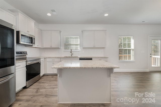 kitchen with white cabinetry, sink, light stone counters, a kitchen island, and appliances with stainless steel finishes