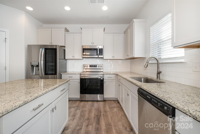 kitchen featuring sink, light hardwood / wood-style flooring, light stone counters, white cabinetry, and stainless steel appliances