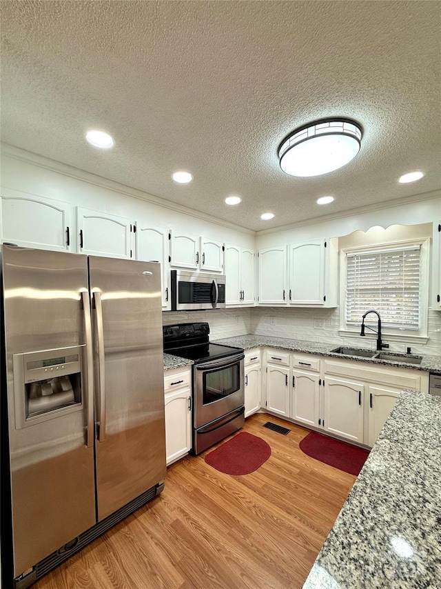 kitchen with sink, light stone countertops, light hardwood / wood-style floors, white cabinetry, and stainless steel appliances