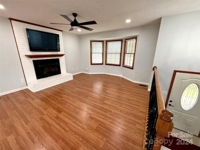 unfurnished living room featuring a textured ceiling, light hardwood / wood-style floors, a brick fireplace, and ceiling fan