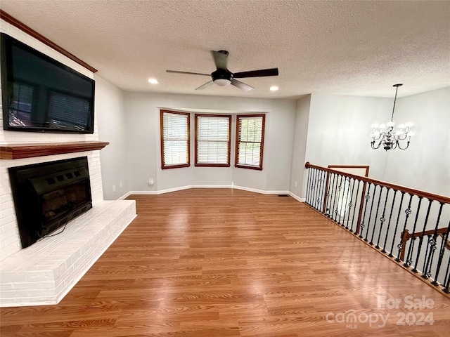 unfurnished living room with hardwood / wood-style flooring, a textured ceiling, and a brick fireplace