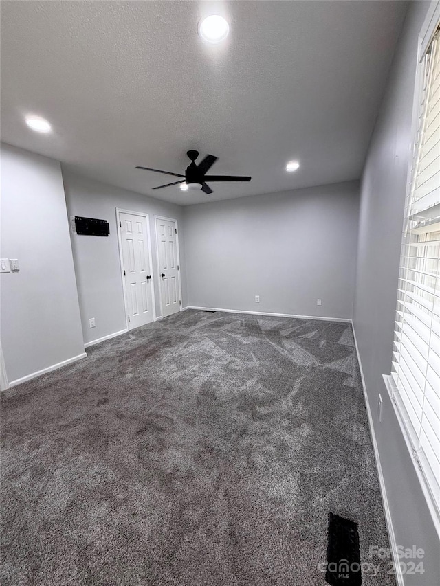 unfurnished bedroom with dark colored carpet, ceiling fan, a textured ceiling, and multiple closets