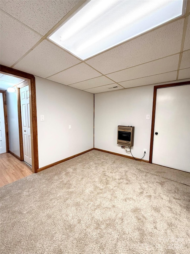 basement featuring heating unit, light carpet, and a drop ceiling